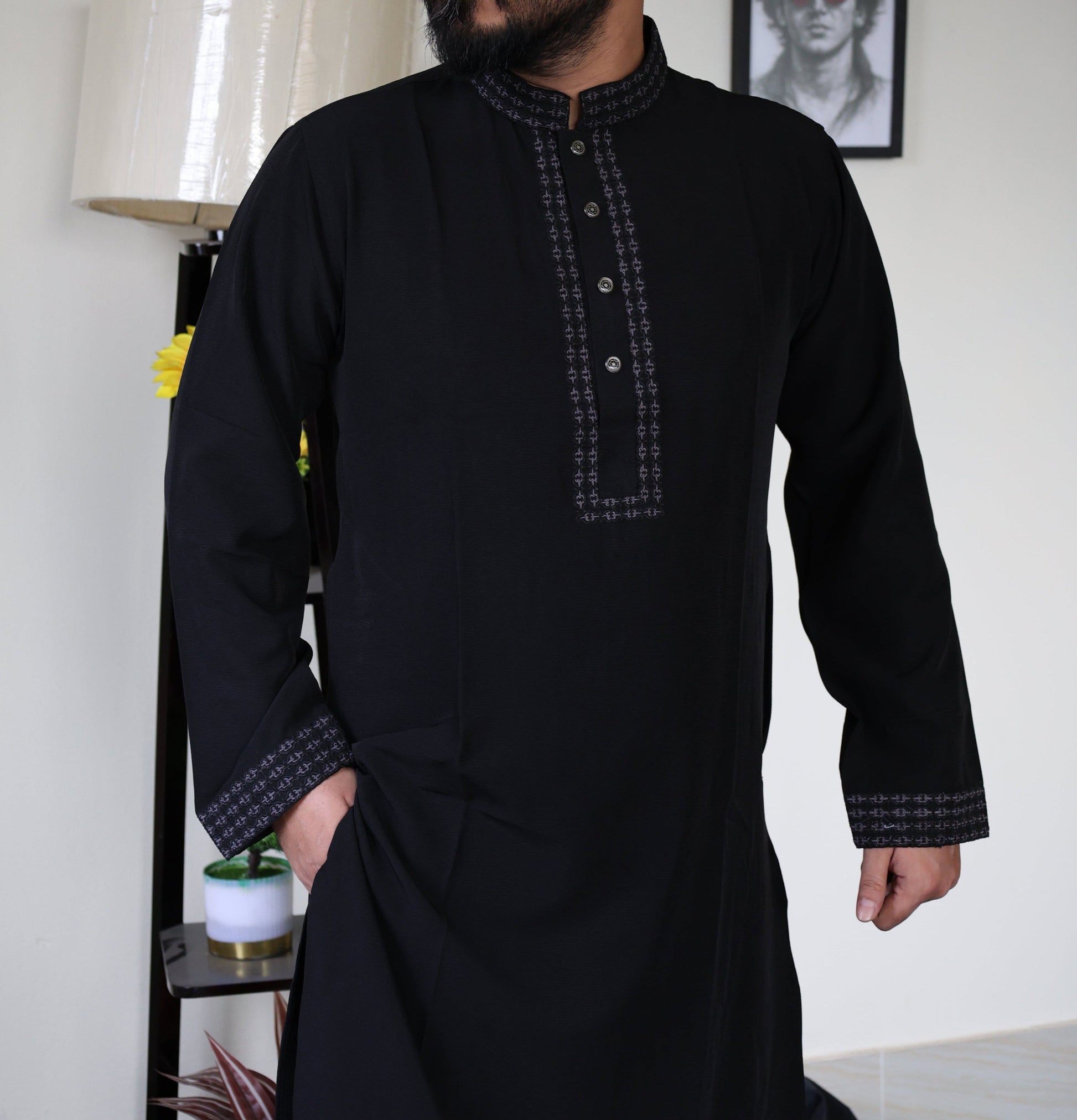 Person wearing a black traditional outfit with intricatghhe patterns in a room setting.