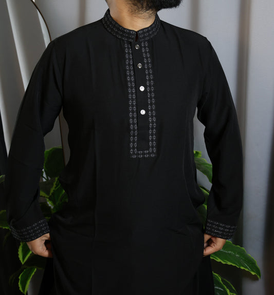 Person wearing a black kurta with intricate embroidery against a neutral background